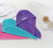 Three Turbie twist hair towels laying on a flat surface, with bath accessories